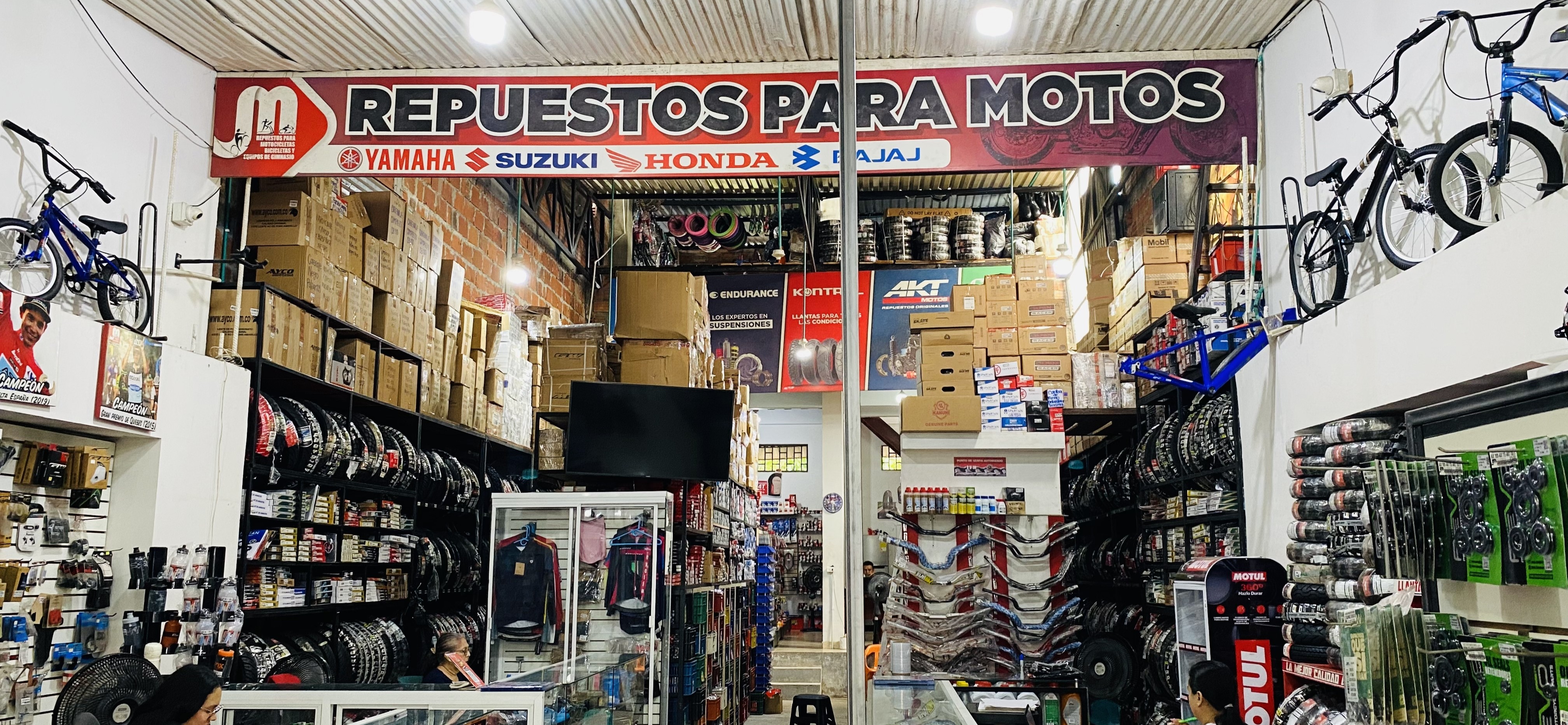 Interior de JM Repuestos con letrero Repuestos para Motos, bicicletas colgadas y estanterías de llantas