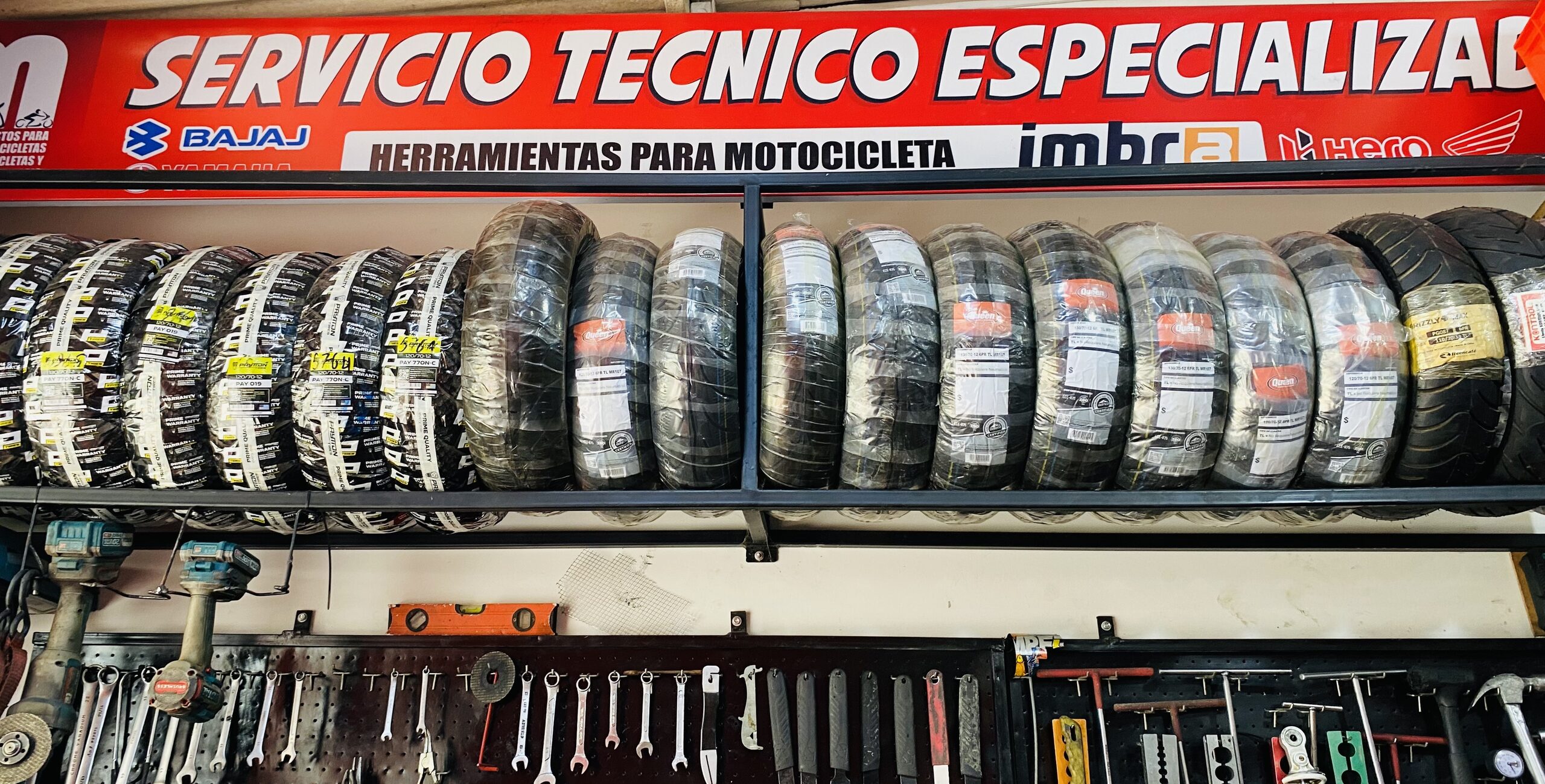 Estantería de llantas para motocicleta con letrero de servicio técnico especializado y herramientas en JM Repuestos